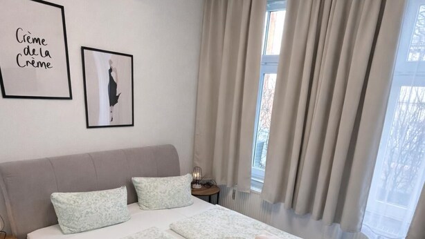 Een slaapkamer met een groot bed, twee kussens, een nachtkastje met een lamp en een raam met gordijnen.