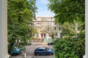 Reih von Reihenhäusern mit einer Straße davor, Bäumen an beiden Seiten und geparkten Autos.