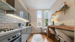 Eine moderne Küche mit Gasherd, Mikrowelle und Backofen, ein Essbereich mit Holztisch und Stühlen sowie ein Blick auf die Stadt durch große Fenster.