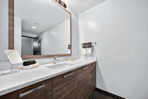 A modern bathroom with a large mirror, a sink, and wooden cabinets. - Modern Downtown Apartment | Pool, Laundry, Valet Parking (Dallas)