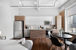 A modern kitchen with stainless steel appliances, wooden cabinets, and a large window offering a city view. - Modern Downtown Apartment | Pool, Laundry, Valet Parking (Dallas)