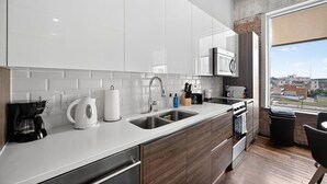 Une cuisine moderne avec des armoires blanches, des appareils en acier inoxydable et une grande fenêtre donnant sur la ville.