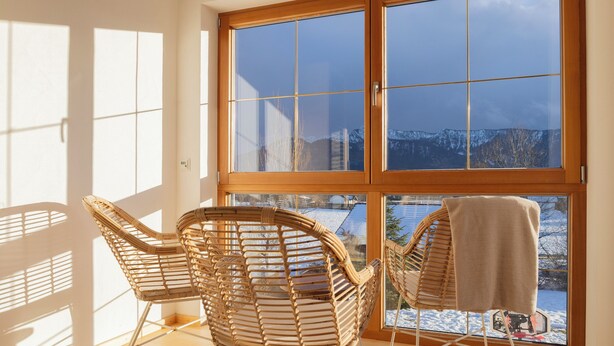 A room with large windows, wicker chairs, and a view of a snowy landscape. - ღLiboria | Bright balcony apartment by the lake (Riegsee)