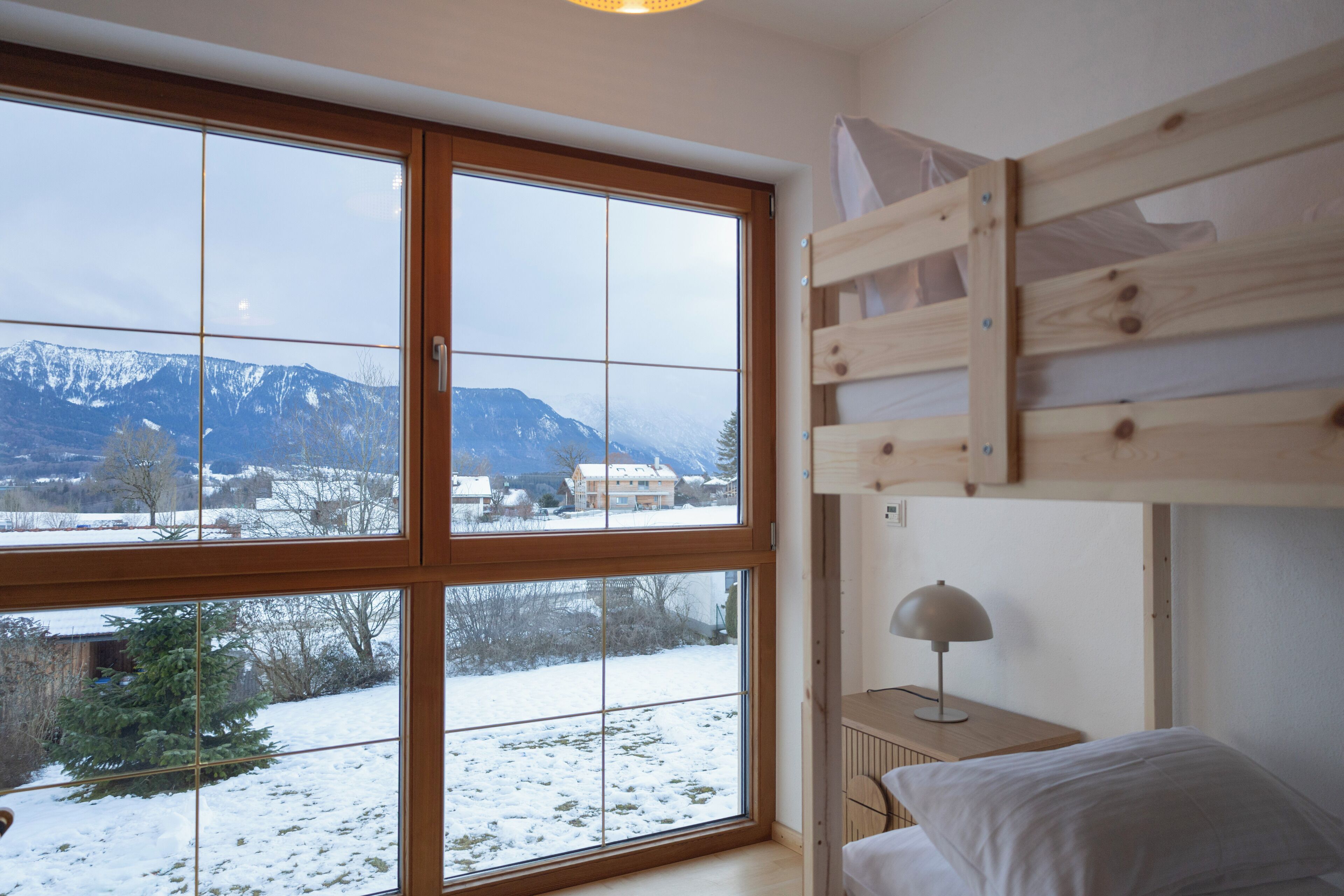 Una habitación con literas, ventanas amplias que dan a un paisaje nevado y una mesita de noche con lámpara.