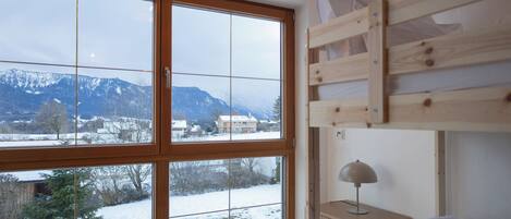 Una habitación con literas, ventanas amplias que dan a un paisaje nevado y una mesita de noche con lámpara.