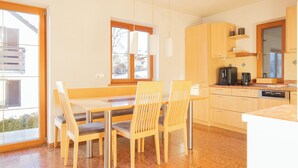 A modern kitchen with a dining area, featuring a large window, wooden cabinets, and stainless steel appliances. - ღLiboria | Bright balcony apartment by the lake (Riegsee)