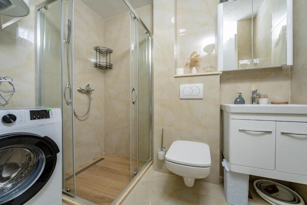 Un baño moderno con ducha de vidrio, inodoro, lavadora y tocador con espejo.