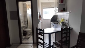 Een kleine keuken met een eethoek, witte betegelde wanden en een raam dat voor daglicht zorgt.