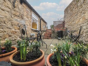 A stone building with a patio area featuring a table and chairs, surrounded by potted plants. - Daisy Cottage (Pickering)