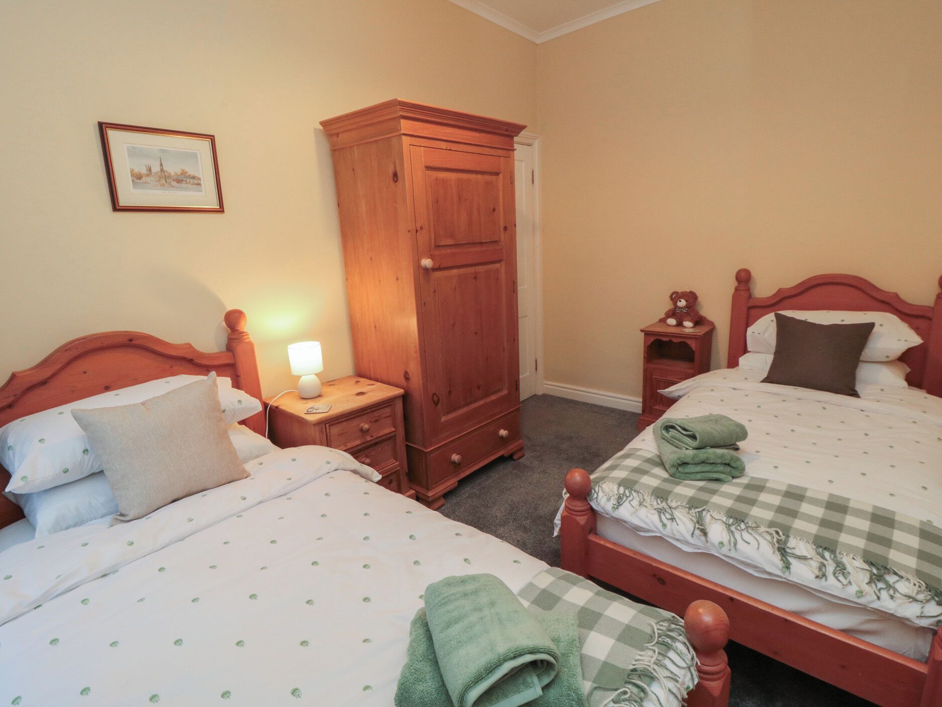 Une chambre avec deux lits, une armoire, une table de chevet avec une lampe et un tableau encadré au mur.