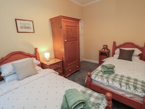 A bedroom with two beds, a wardrobe, a nightstand with a lamp, and a framed picture on the wall. - Daisy Cottage (Pickering)