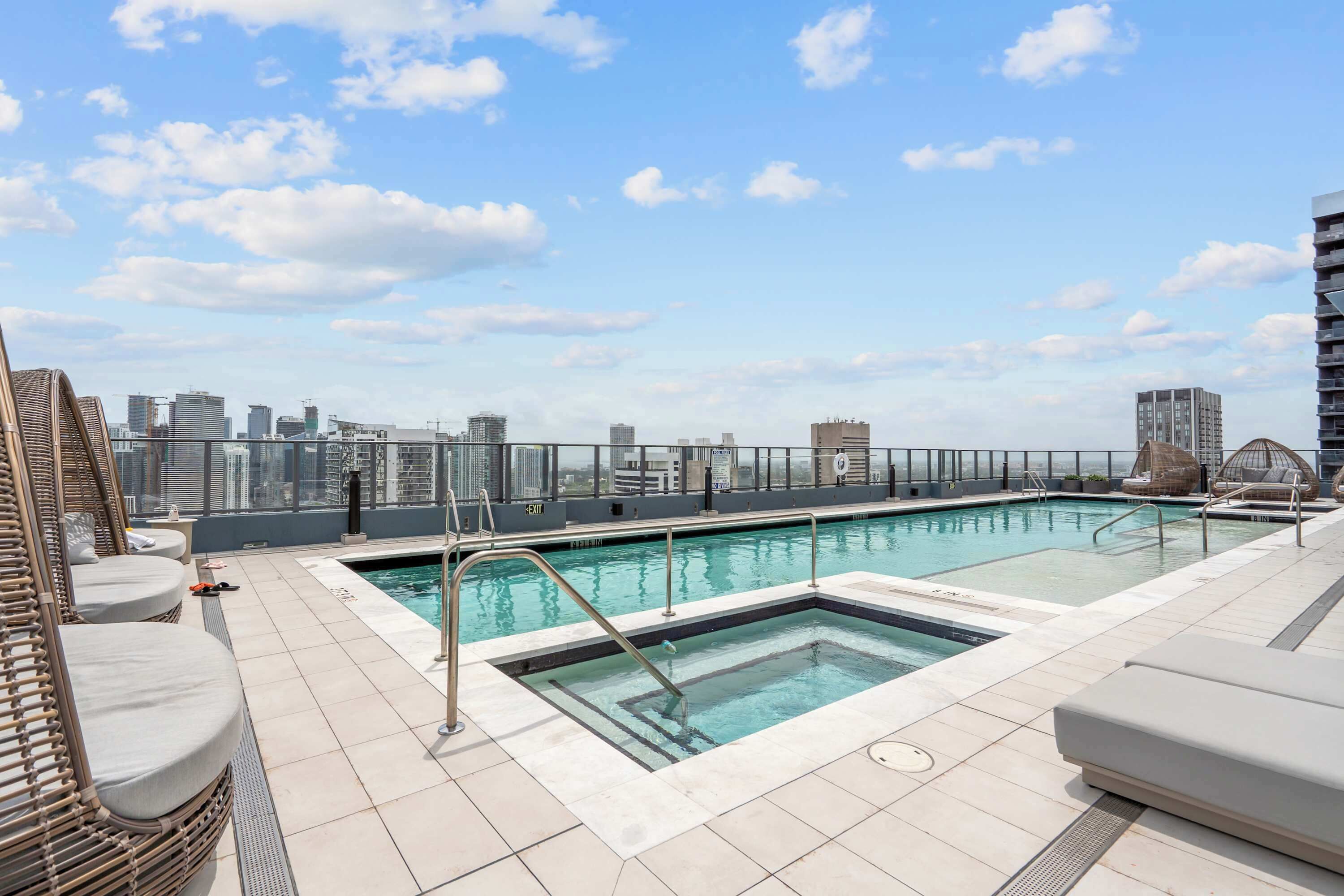 Une piscine sur le toit offrant une vue panoramique sur la ville, des chaises longues et un design moderne.