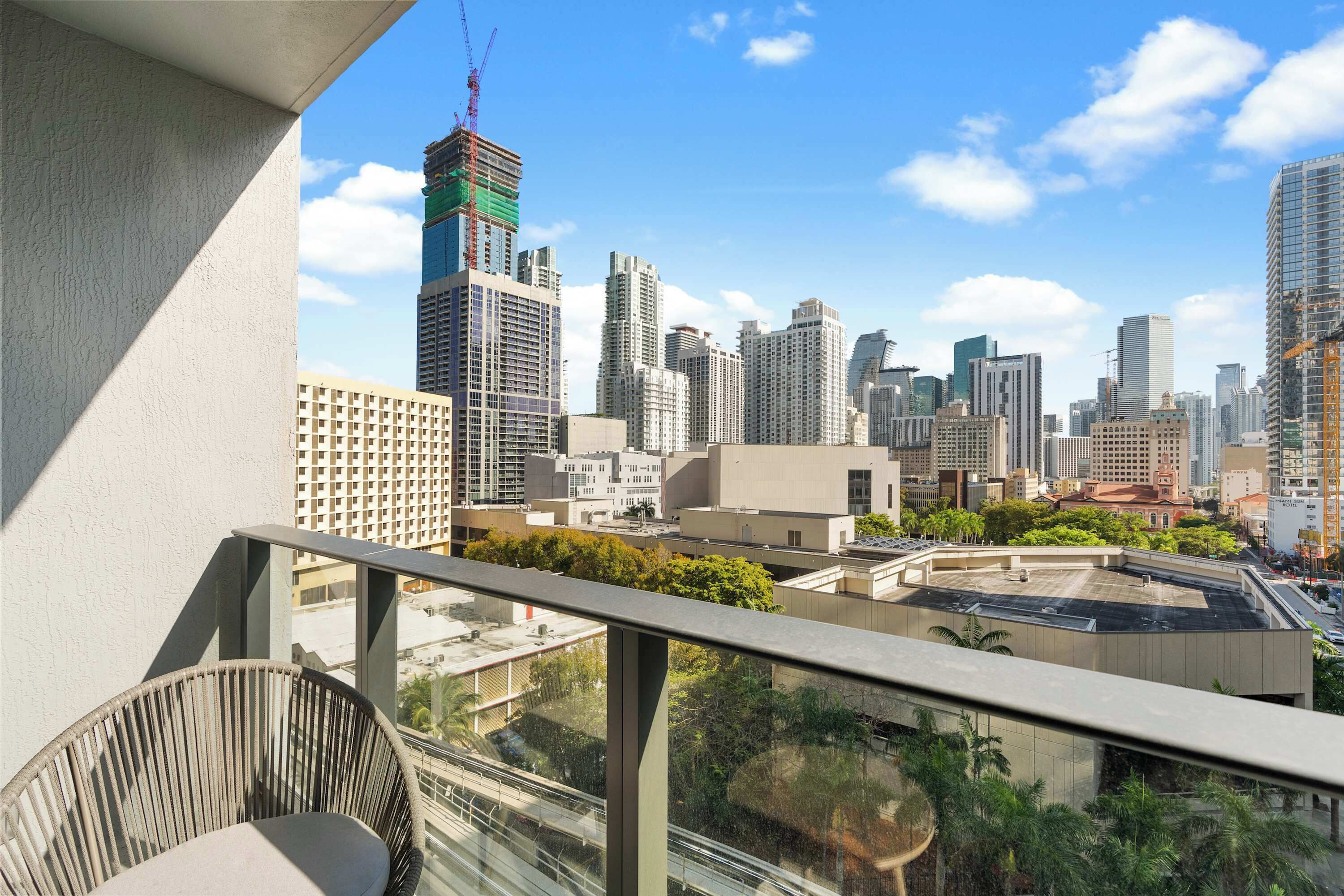 Un balcon offrant une vue sur le paysage urbain, avec notamment des immeubles de grande hauteur et des grues de chantier.
