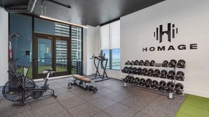 Ein Fitnessraum mit Trainingsgeräten, einer Bank und einem an der Wand befestigten Hantelständer.