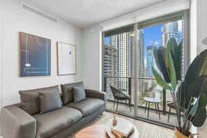 Ein modernes Wohnzimmer mit einem grauen Sofa, einem runden Couchtisch und einem großen Fenster mit Blick auf hohe Gebäude.