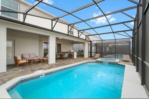 A swimming pool with a glass enclosure, outdoor seating, and a patio area. - Luxury 8BR Home w Game Room Pool Windsor Cay (Clermont)