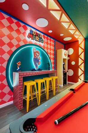Een levendige kamer met een Super Mario thema, inclusief een neonbord, een bakstenen muur, gele krukken en een pooltafel.