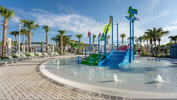 Parque acuático con toboganes y zona de piscina rodeada de palmeras y sillas de descanso.