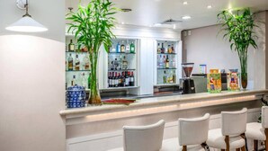 A bar area with a counter, shelves of liquor bottles, two potted plants, and white chairs. - Hotel Blue Tree Premium by Wecare (São Paulo)