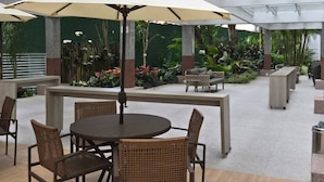 An indoor patio area with round tables and chairs, a large umbrella, and potted plants. - Hotel Blue Tree Premium by Wecare (São Paulo)
