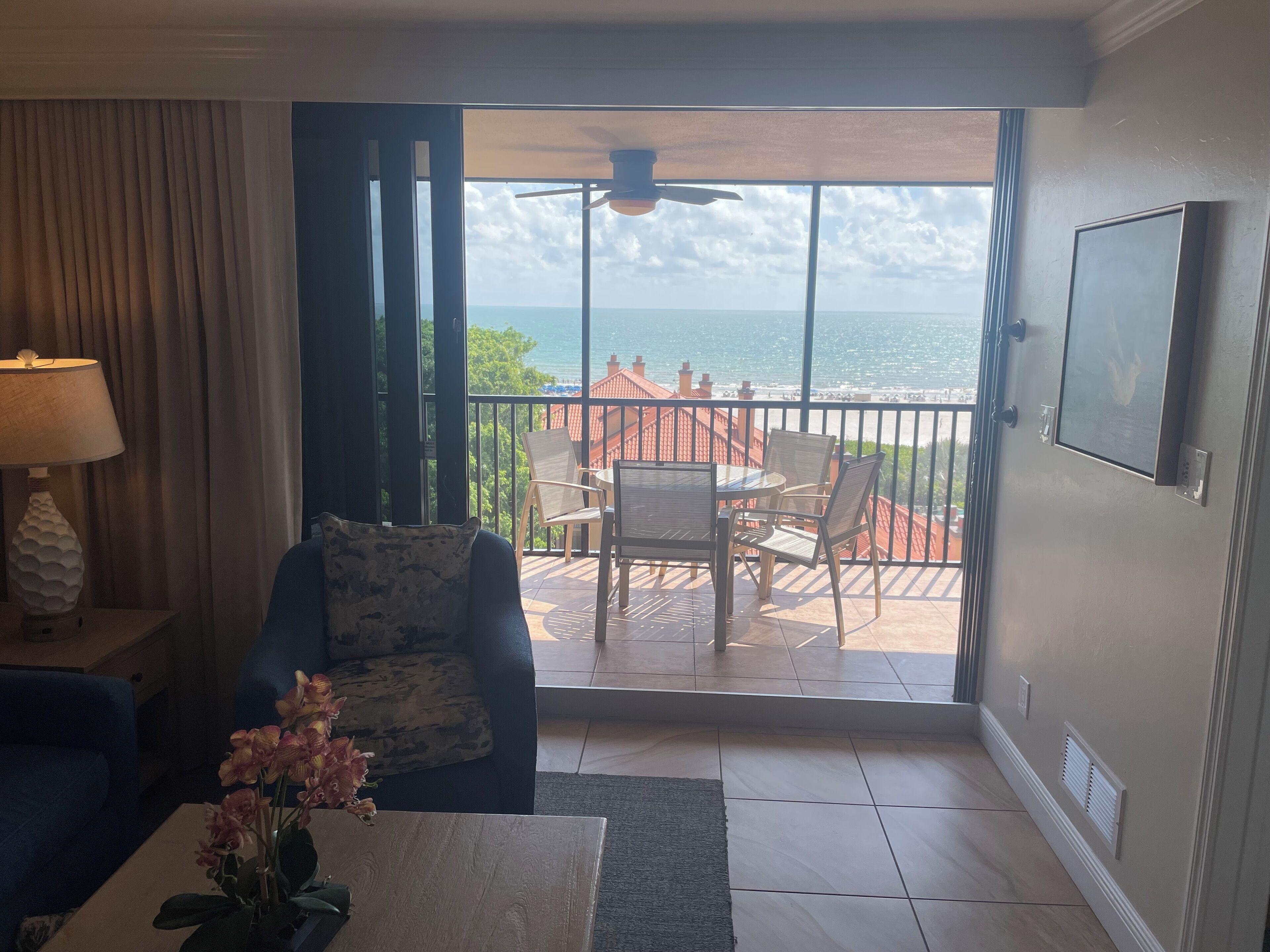 A living room with a view of the sea, a ceiling fan, and a dining area with chairs and a table.