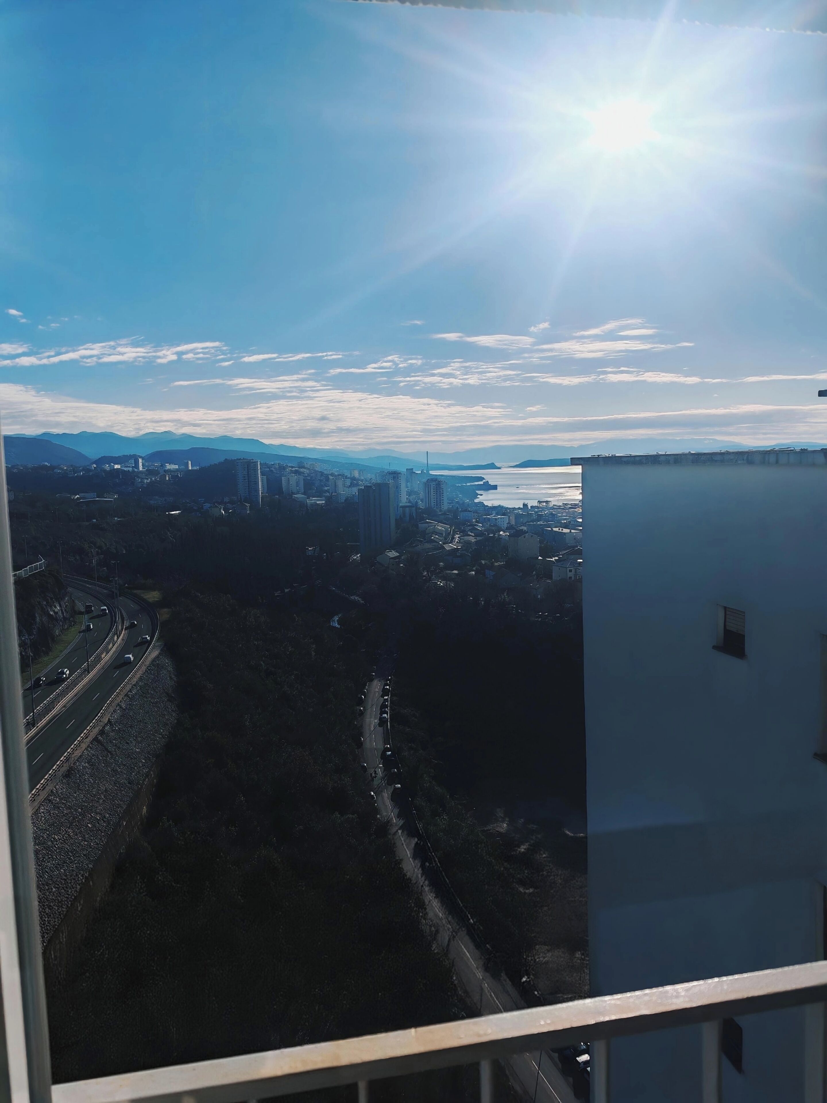 A high-rise building with a view of a cityscape, including a body of water and mountains in the distance.