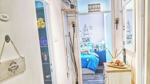 En smal hall med ett kaklat golv leder in till ett sovrum med en säng och ett fönster.