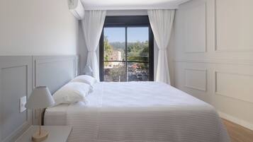 Ein Schlafzimmer mit Bett, Nachttisch, Lampe, Fernbedienung und einem Fenster mit Vorhängen.
