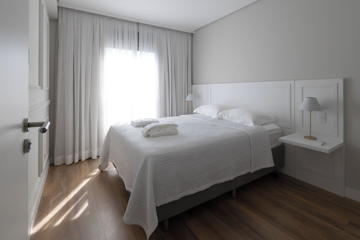 A bedroom with a bed, a nightstand, a lamp, and a window with curtains.