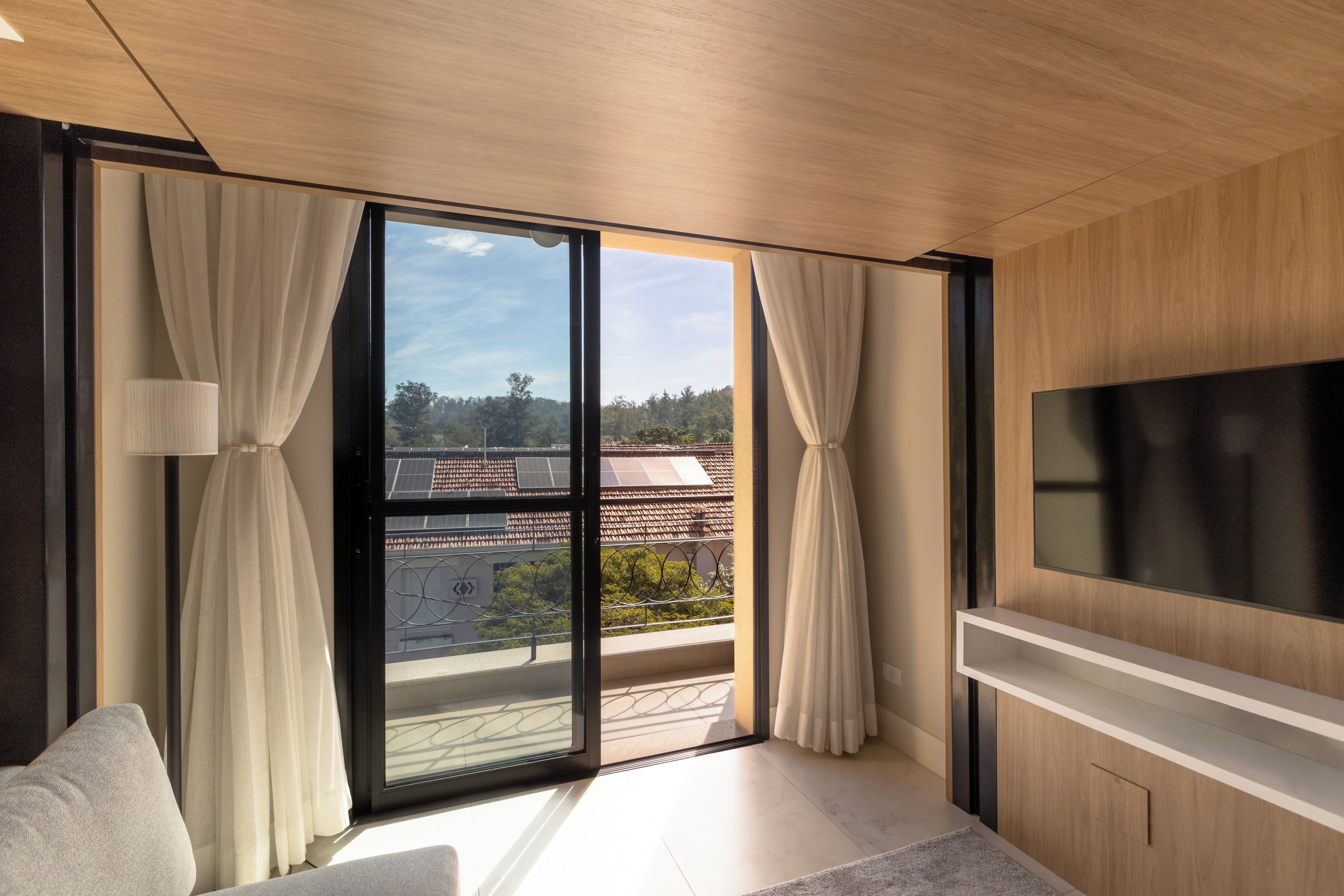Una habitación moderna con un televisor grande, puertas de cristal correderas a un balcón y un sofá.