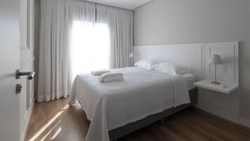 Un dormitorio con cama, mesita de noche, lámpara y ventana con cortinas.