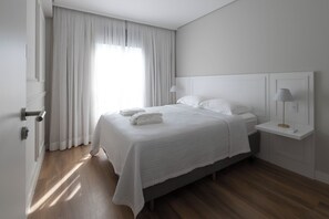 Un dormitorio con cama, mesita de noche, lámpara y ventana con cortinas.
