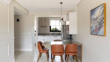 Una cocina moderna con armarios blancos, una mesa de comedor de cristal y tres sillas naranjas.