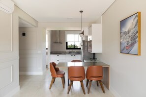 Una cucina moderna con mobili bianchi, un tavolo da pranzo in vetro e tre sedie arancioni.