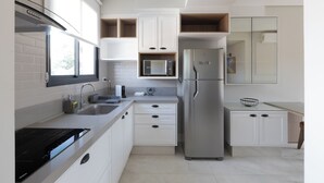 A modern kitchen with white cabinetry, a stainless steel refrigerator, a microwave, and an induction cooktop. - 1986 Apparts  (Águas de São Pedro)