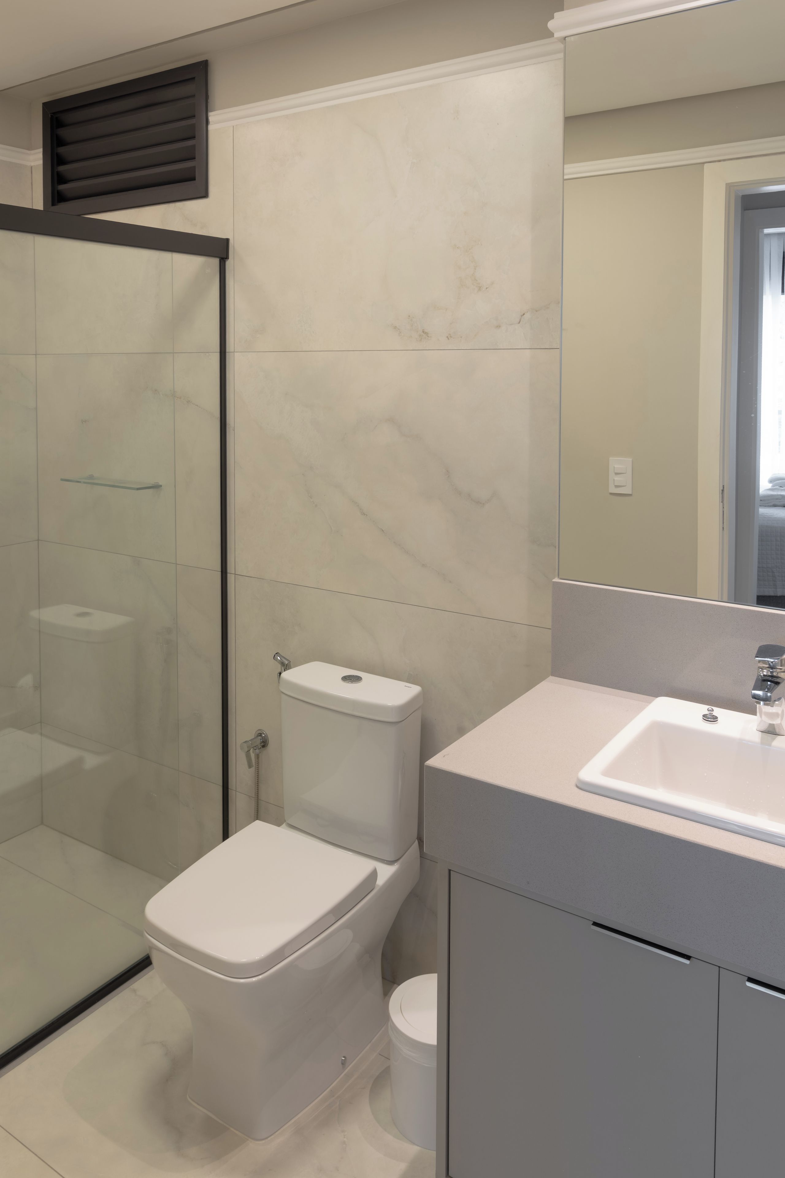 A bathroom with a glass shower enclosure, a toilet, and a sink with a mirror above it.