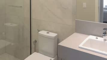 A bathroom with a glass shower enclosure, a toilet, and a sink with a mirror above it.