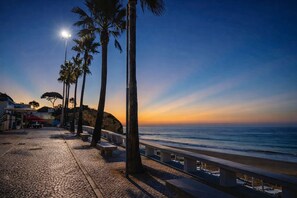 A coastal walkway with benches, palm trees, and a sunset view. - Varandas do Mar Patricia (Olhos de Agua)