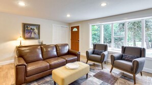 A living room with a brown leather sofa, two armchairs, a small ottoman, a framed painting, and a door.