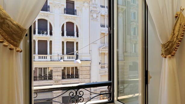 Una finestra con tende elaborate, una ringhiera da balcone e vista su un edificio dall'architettura classica.