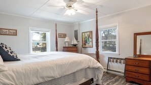 Une chambre à coucher avec un lit à baldaquin, une commode en bois, un ventilateur de plafond et une fenêtre donnant sur l’extérieur.