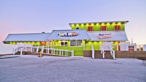 Un bâtiment à la façade verdoyante, une enseigne indiquant « Surf's Up! Bar », et un escalier menant à l’entrée.