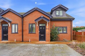 A row of three brick houses with black doors and windows, a paved driveway, and a clear sky. - Modern Ensuite Home with Drive and easy M6 Access (Wednesbury)