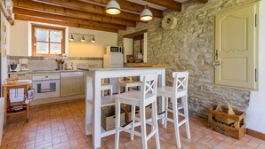 Una cocina rústica con vigas de madera, una pared de piedra, una mesa blanca con sillas y un microondas.