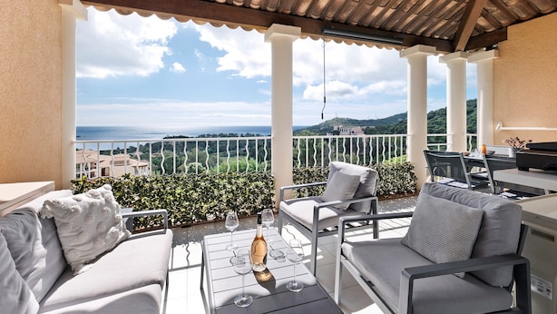 Ein Balkon mit Meerblick, Gartenmöbeln und einem Tisch mit Weingläsern und einer Weinflasche.