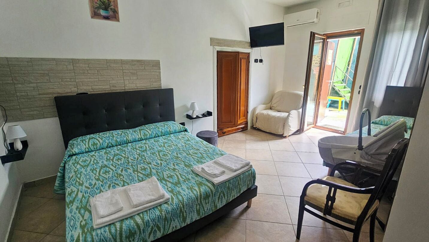 A hotel room with a bed, a chair, a TV, and a door leading to a balcony.