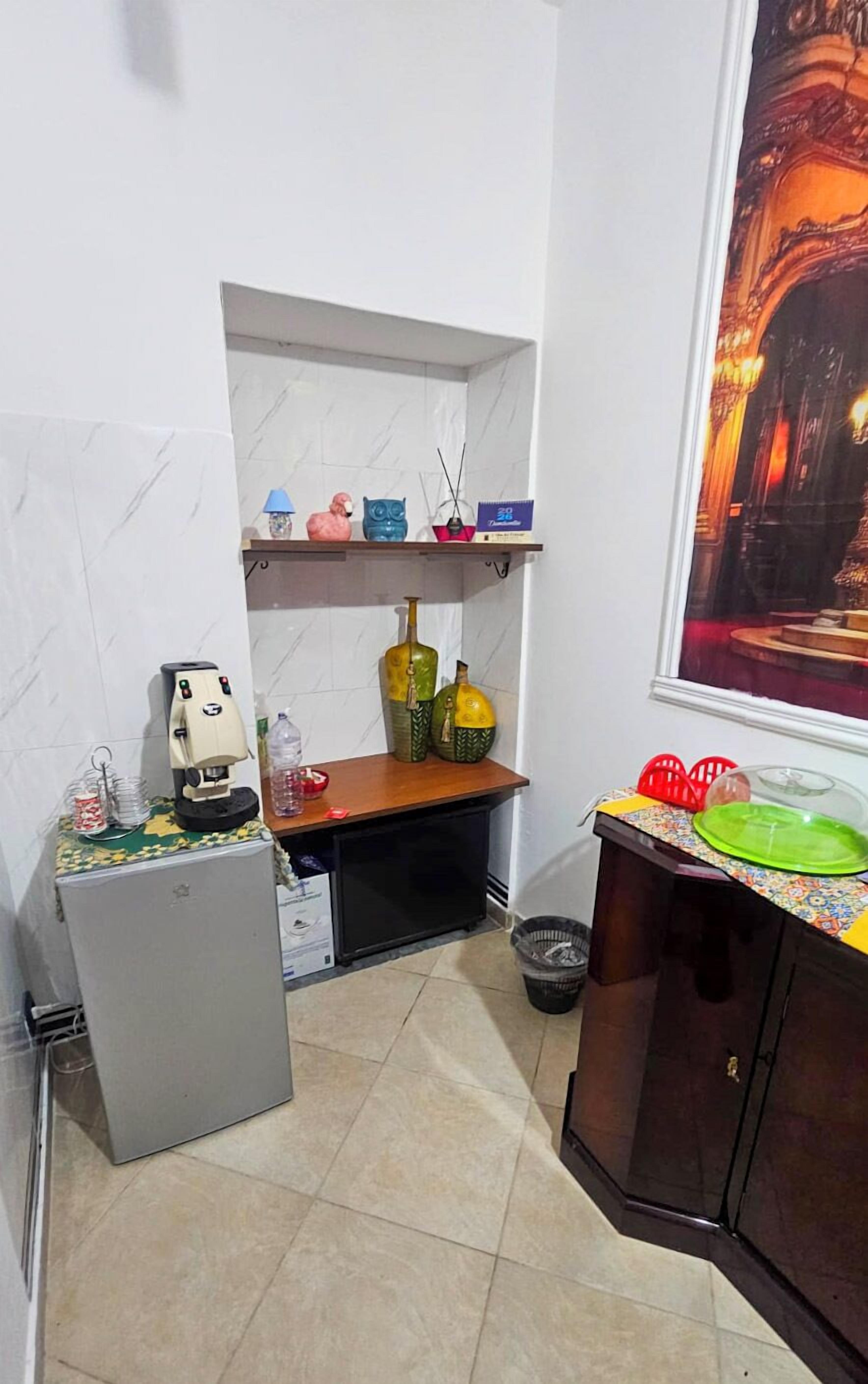 Una cocina compacta con refrigerador, cafetera, lavamanos y ventana con vista a un edificio.