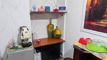Una cocina compacta con refrigerador, cafetera, lavamanos y ventana con vista a un edificio.