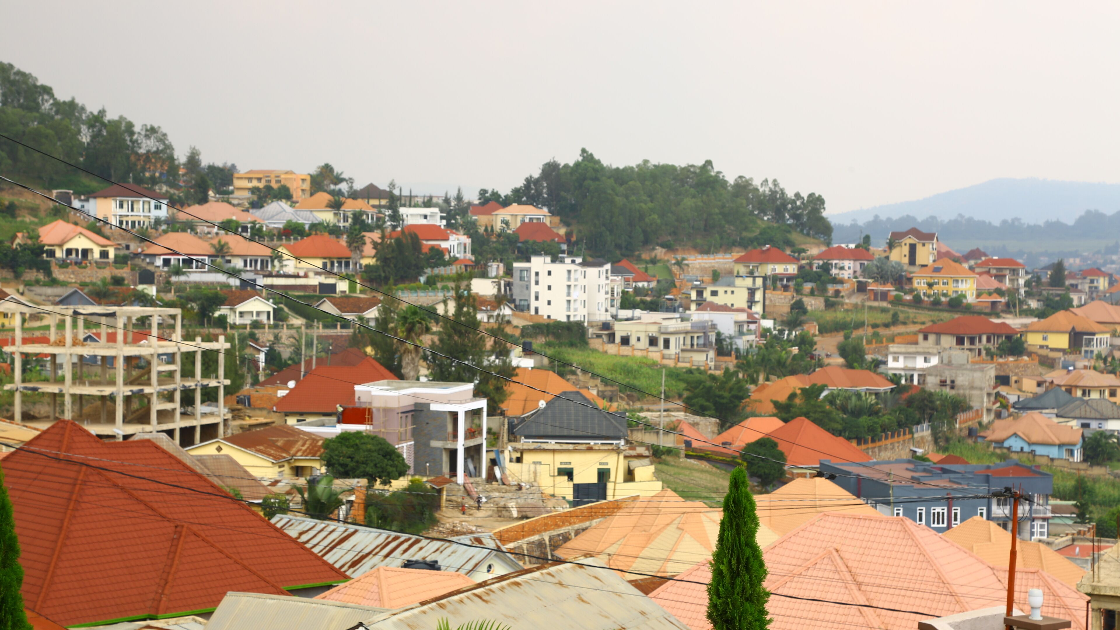 A residential area with various houses and buildings, some under construction, and a hilly backdrop.