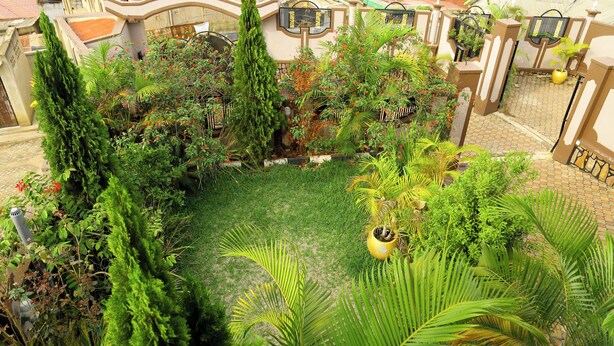 A lush garden with various plants and a central grassy area, surrounded by a decorative fence. - KIGALI BRIGHT HOMES AND HOTEL (Kigali)